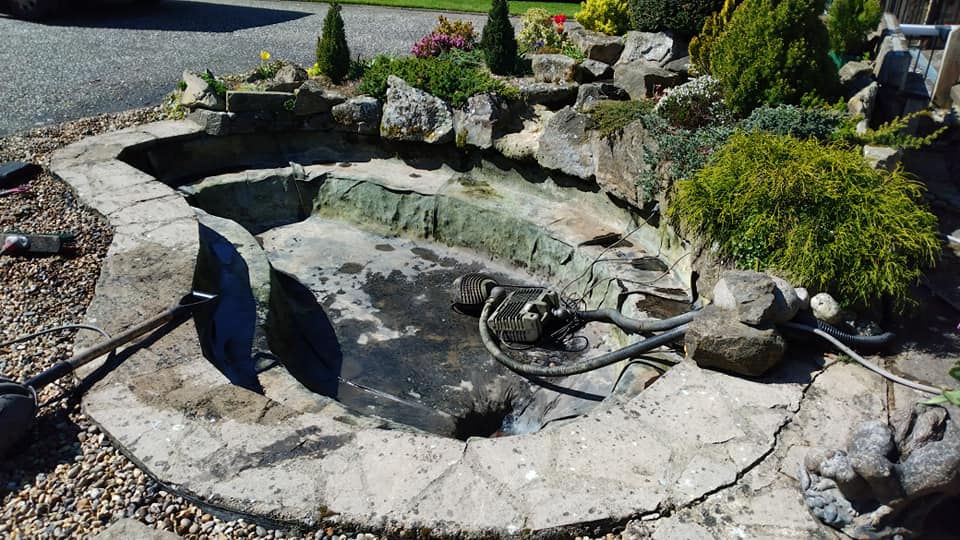 Drained slab rimmed natural shaped pond freshly cleaned ready to be refilled