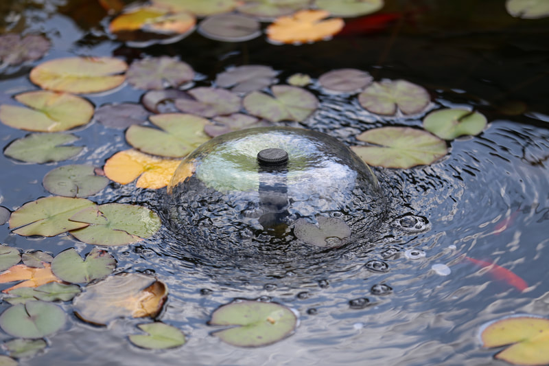 Close up of a pond dome fountain surrounded by water lily pads